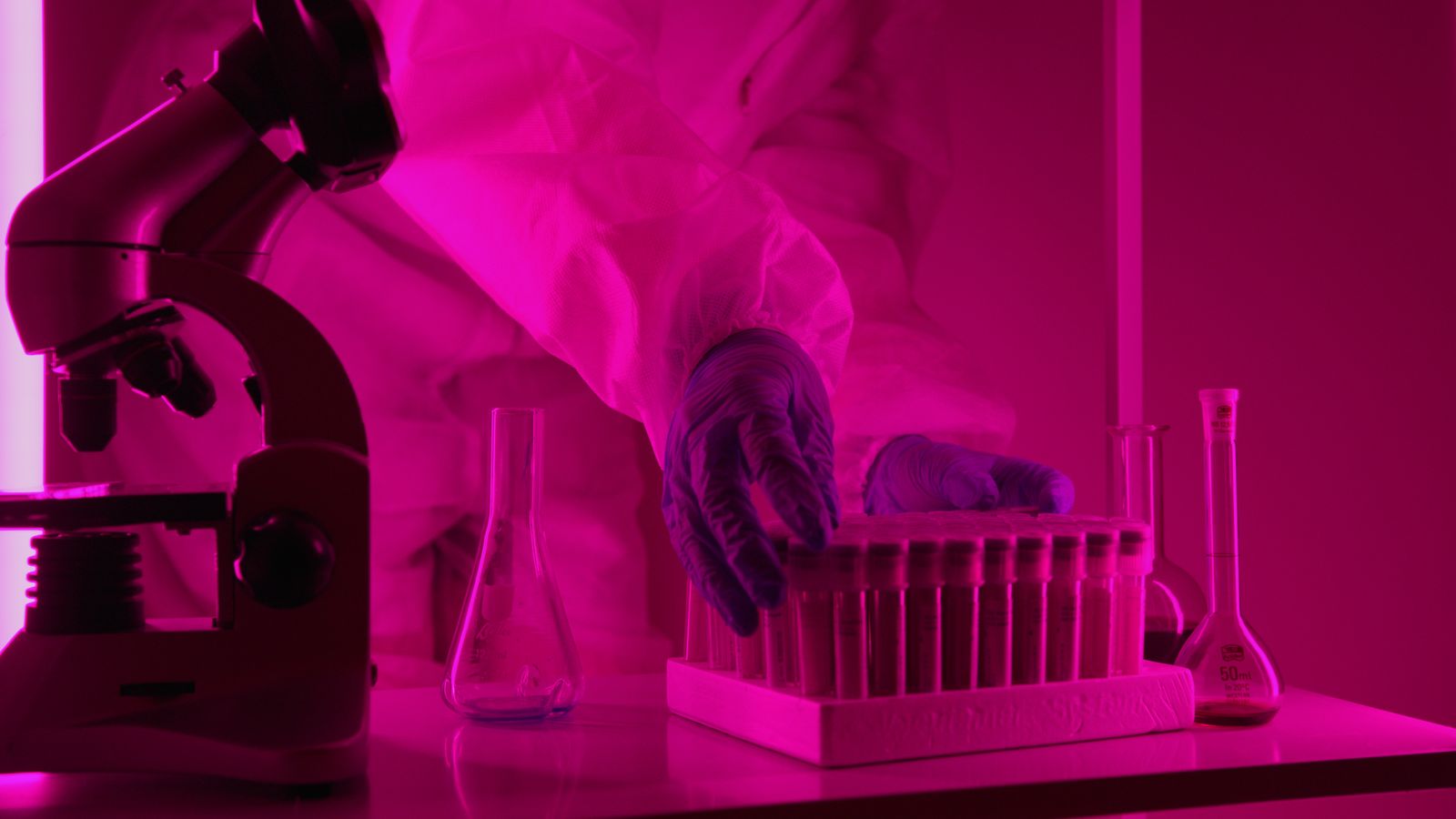 Scientist handling test tubes in a pink-lit laboratory